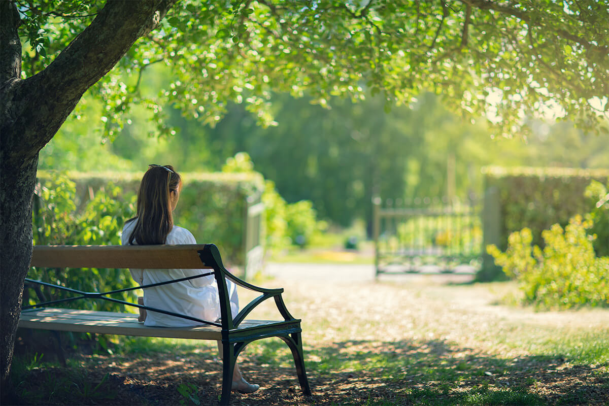 A woman sitting in a bench under the shade. No image credit.