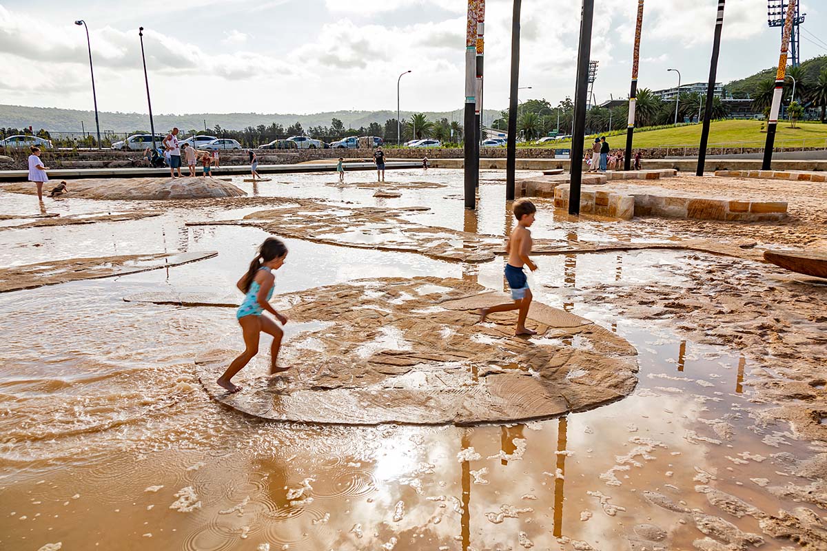 Children play on sandstone shapes in shallow water play area at Gosford Waterfront Park. Credit: Guy Wilkinson