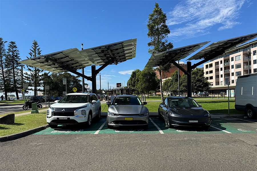 A carpark with three electric vehicles parked under electric vehicle charging panels. Credit: Department of Climate Change, Energy, the Environment and Water