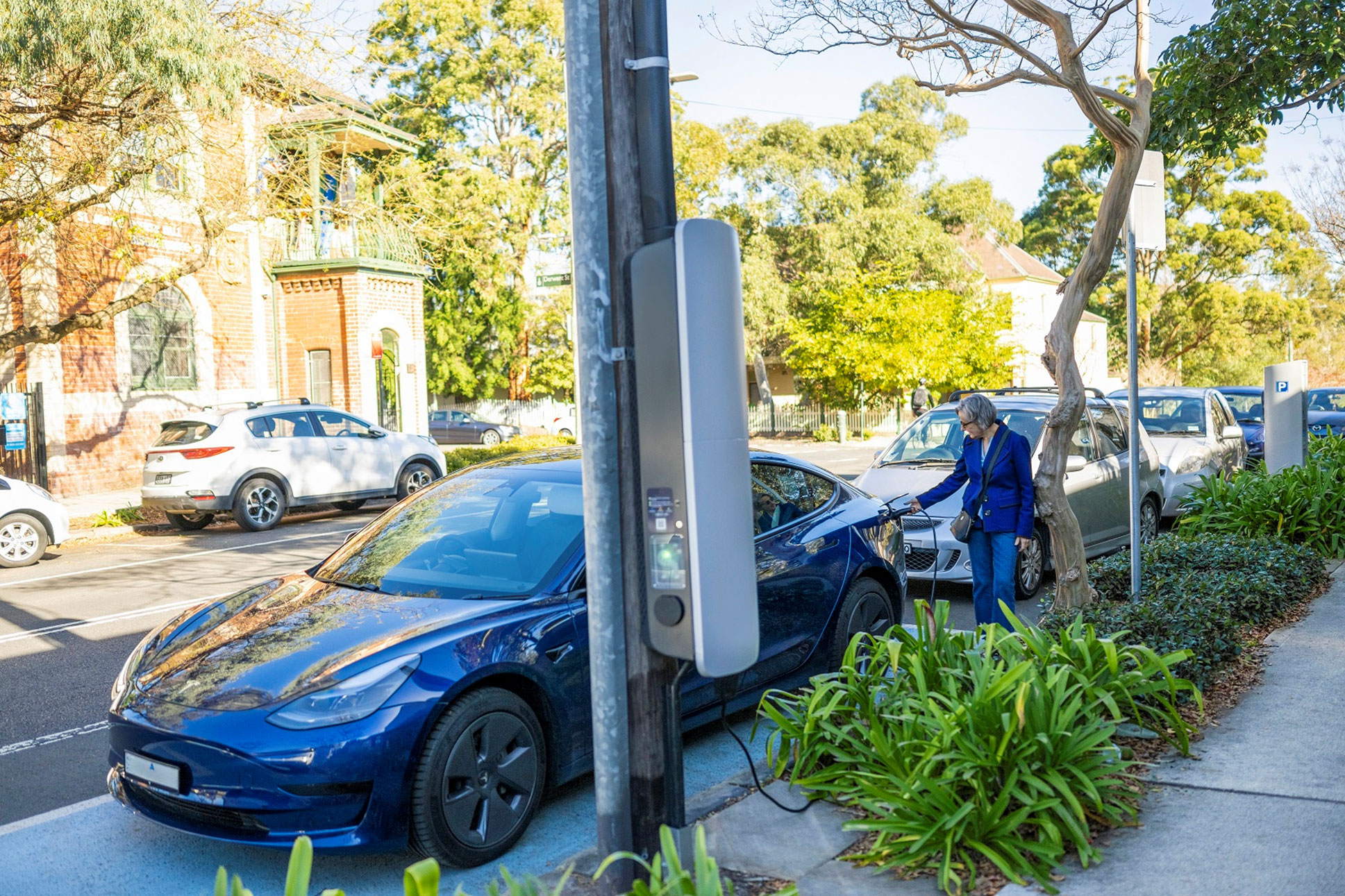 A person charging an electric vehicle from a charger mounted to a pole beside the road. Credit: Jessica Lindsay / Department of Climate Change, Energy, the Environment and Water