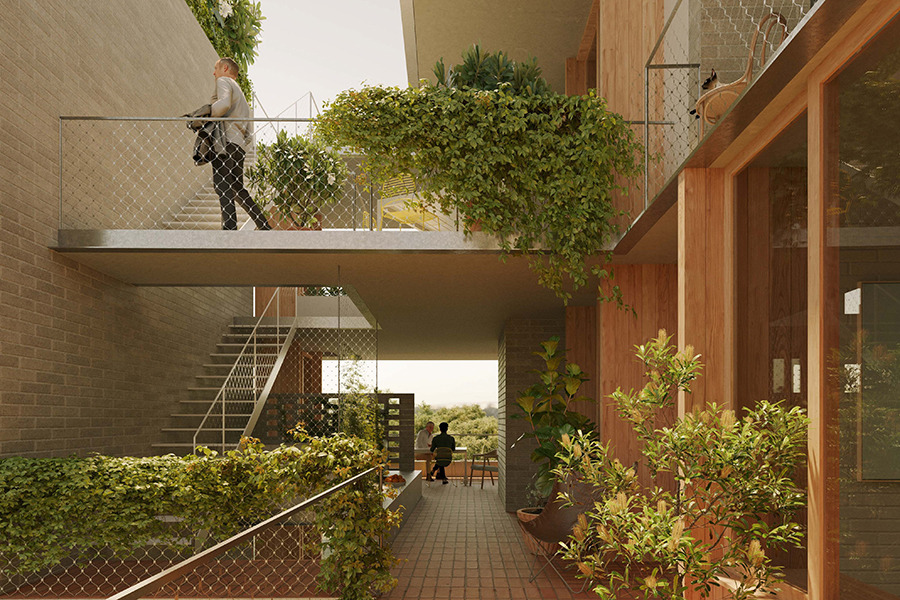 The outdoor shared corridor space of a mid-rise apartment. The building is brick and there are timber door and window frames and metal railings along the walkways. There are 2 levels visible. A person walks along the upper level walkway. Two people seat at a seat in the background. Both levels are above ground and trees and sky can be seen in the background.