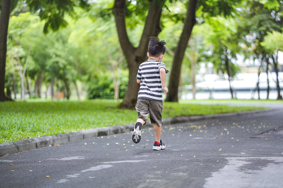 Child running down a shaded path in a park.