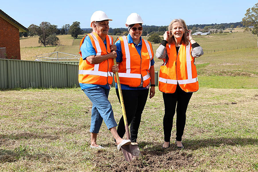 Three people wearing protective equipment turning sod at Bowraville Reserve.