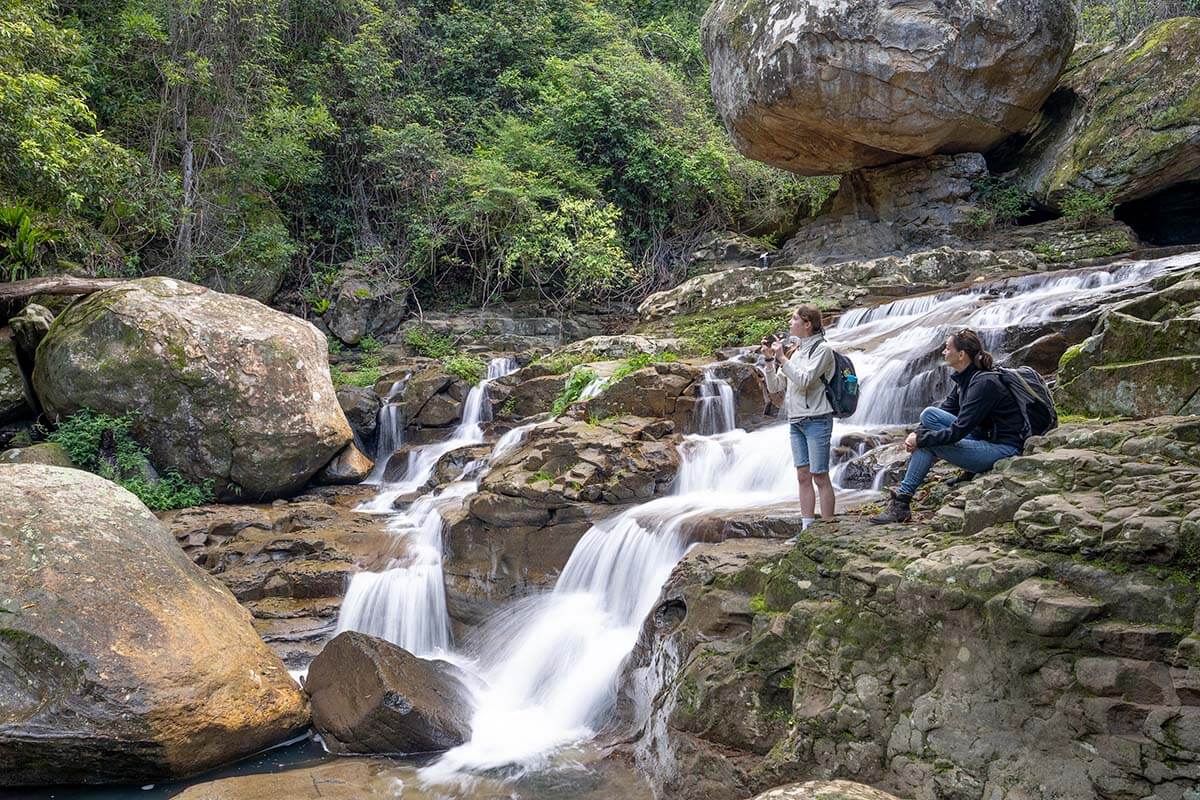 Two people admiring a waterfall at Macquarie Pass in the Illawarra Shoalhaven region of NSW. Credit: NSW Department of Planning, Housing and Infrastructure